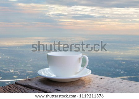 a selective focus picture of a cup of coffee on wooden table beside terraced house near cliff edge. 