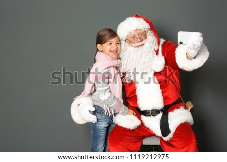 Authentic Santa Claus taking selfie with little girl on grey background