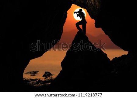 Photographer in front of the cave near the sea with red sky sunset background.