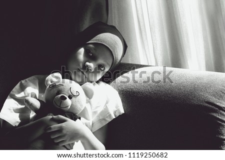 Black and white image of Patient kid lie down on couch with doll.Girl cover her head with headscarf.Kid look sad,tired and sick.Concept of   childhood cancer awareness.Selective focus.