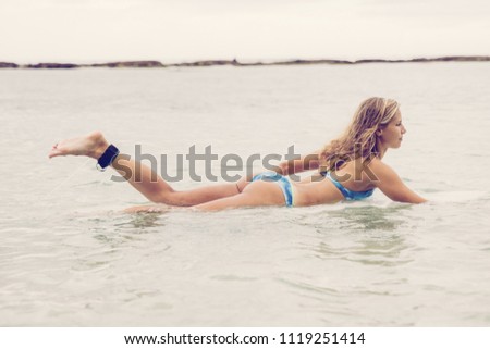 Young beautiful woman swimming on surfboard in sea. Side view.