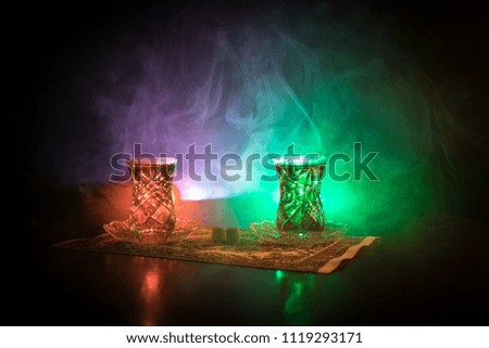 Eastern tea in traditional glasse and pot on black background with lights and smoke. Eastern tea concept. Armudu traditional Azerbaijan/Turkish cup. Selective focus. Glass of Tea