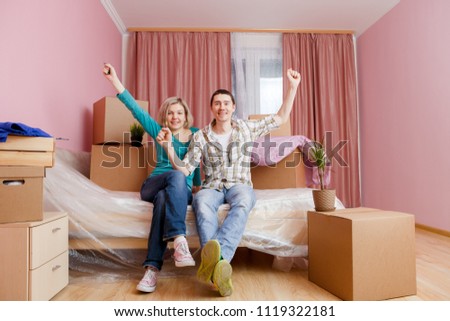 Photo of happy men and women sitting on bed among cardboard boxes