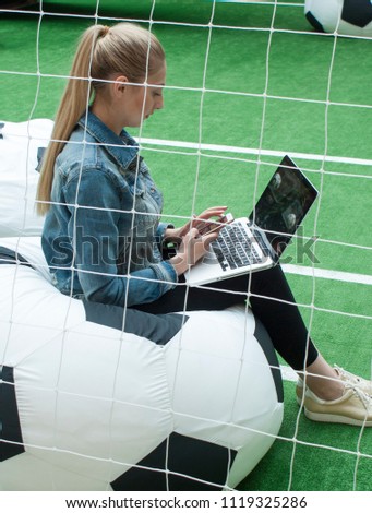Girl with phone and laptop on the football field
