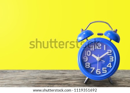 Concept with blue alarm clock on wood table with yellow background. copy space for text and design.