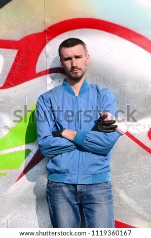 The graffiti artist with spray can poses against the background of a colorful painted wall. Street art concept