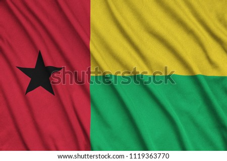 Guinea Bissau flag  is depicted on a sports cloth fabric with many folds. Sport team banner