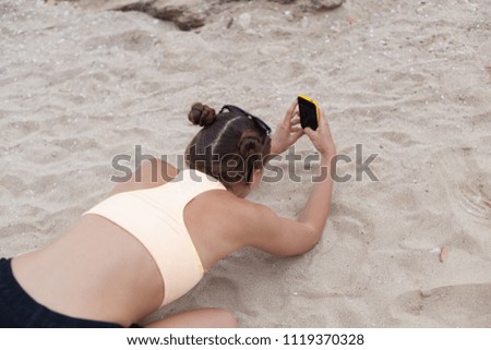 Beautiful woman taking photos on yhe knees with smart phone technology on paradise beach destination summer wanderlust vacation.