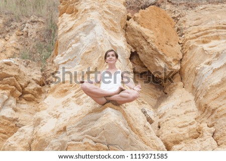A beautiful young girl with short hair is dressed in shorts and a white jersey is practicing yoga on the background of rocks. Pose of the lotus. The concept of calm and concentration.