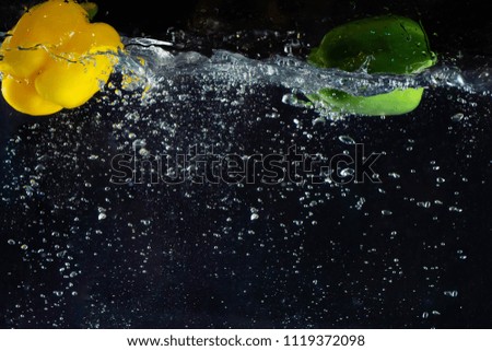 Fresh Vegetable a bell chilli yellow and green color dropping in the water and creating a splash with lot of bubble in black color background.