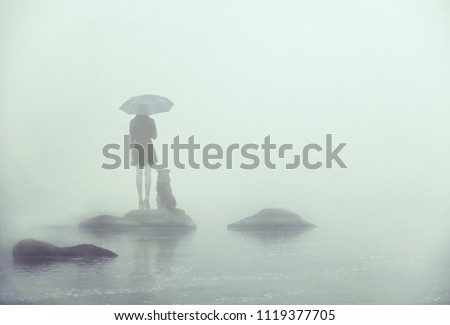 Girl with umbrella and dog standing on a little island in the middle of the water. Lonely in the fog Royalty-Free Stock Photo #1119377705