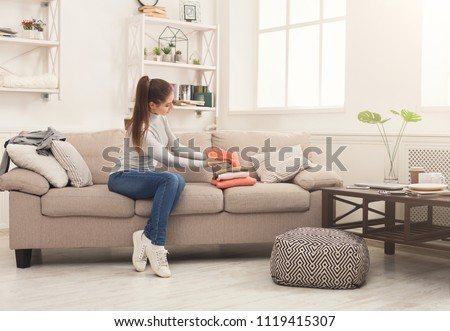 Woman folding clean t-shirts, sitting on sofa at home. Young girl tidying up clothes after laundry or shopping, copy space Royalty-Free Stock Photo #1119415307