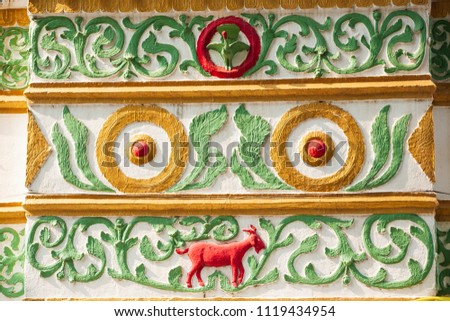 Beautiful vintage exterior. Colorful stucco red goat, green vine and leaves, green peafowl on cream wall. Public temple in Lampang, Thailand. Background, Texture. Traditional spiritual. bright light.