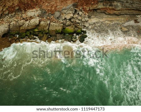 Aerial top view of sea waves hitting rocks on the beach with turquoise sea water. Amazing rock cliff seascape in the Portuguese coastline. Drone shot.