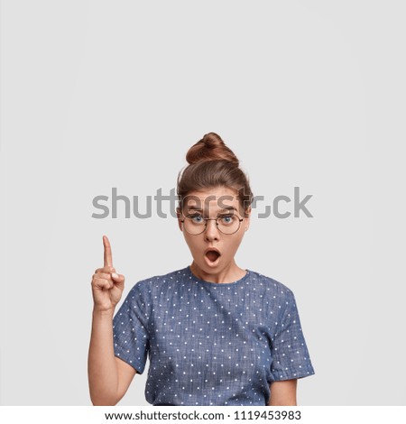 Surprised female model indicates upwards as shows leaking ceiling, looks in bewilderment, dressed casually, stands against white background with copy space for your text. Emotive woman seller