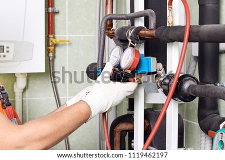 Maintenance engineer checking technical data of heating system equipment in a boiler room. Plumber installing pressure meter for house heating system. Royalty-Free Stock Photo #1119462197