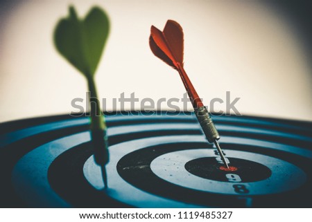 Close up shot of the dart arrow hit on bull eyes of dartboard to represent that the business reached the target of company with dark tone picture style. Target and goal as concept.