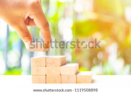 Concepts of building a staircase and step up of wooden pegs for another entrepreneur to climb up the ladder of success.Two finger hold block wood for close project. Royalty-Free Stock Photo #1119508898