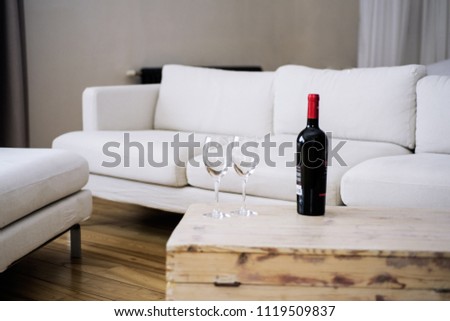 Bottle of Wine on wooden table in empty room with white sofa.  Royalty-Free Stock Photo #1119509837
