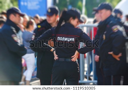 Russian police squad formation back view with "Police" emblem on uniform maintain public order after football game with football fans crowd in the background
