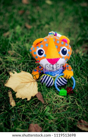 toy tiger of colored knitted fabric sits on grass and holds a sheet in paw