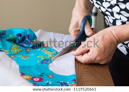 Woman cuts scissors on table with lining of white fabric for dresses