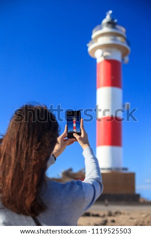 Traveler woman taking photo of lighthouse on beach on Canary Islands, Spain. Travel concept. Destination background