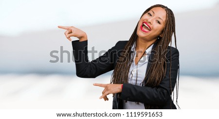 Portrait of a young black business woman pointing to the side, smiling surprised presenting something, natural and casual