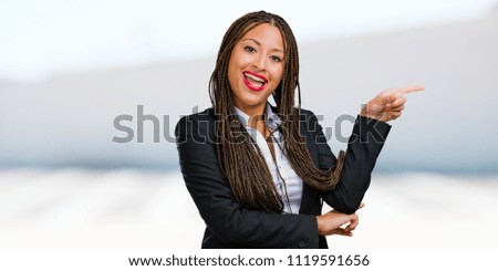 Portrait of a young black business woman pointing to the side, smiling surprised presenting something, natural and casual