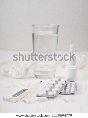 a glass of water, pills, thermometer, paper napkins on white wooden background, Top view, copy space. Medicine concept photo. High angle view, flat lay.