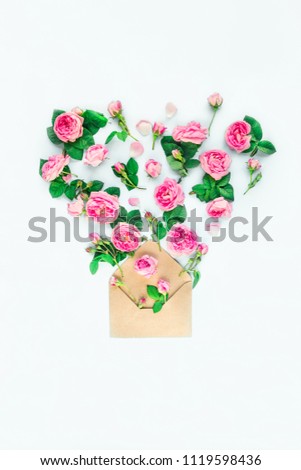 Close up creative layout with pink tea rose flowers,petals, leaves fly out of craft paper envelope in shape of heart on white background isolated. Spring, summer love concept. Copy space
