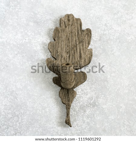 Carved from wood old weathered oak leaf with acorn on light gray concrete background. Minimal style. Vintage autumn concept