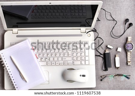 Computer peripherals and laptop accessories. Overhead of modern comfort work place. Green desk with white laptop, mouse ,pen, notebook, usb flash, black mp3 player, eyeglasses and watch.