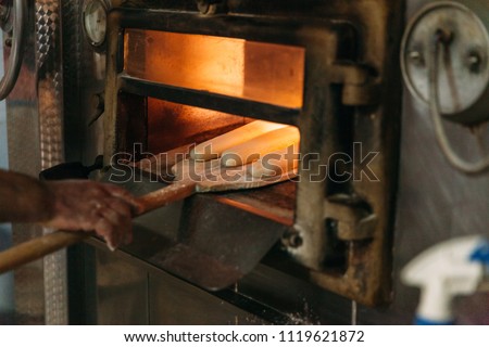 Baker is putting bread in the wood oven. Traditional Bakery Concept.