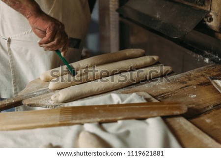 Baker is preparing the raw dough bread before baking in a wood oven. Traditional Bakery Concept.