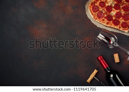 Heart shaped pizza with mozzarella, sausagered with a bottle of wine and wineglas. Valentines day greeting card on rusty background . Top view Royalty-Free Stock Photo #1119641705