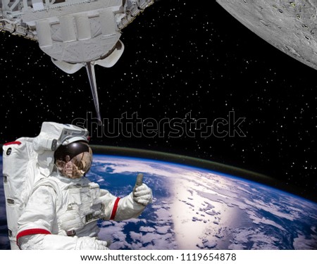 Astronaut gives thumbs-up, earth and planet with craters like moon. The elements of this image furnished by NASA.
