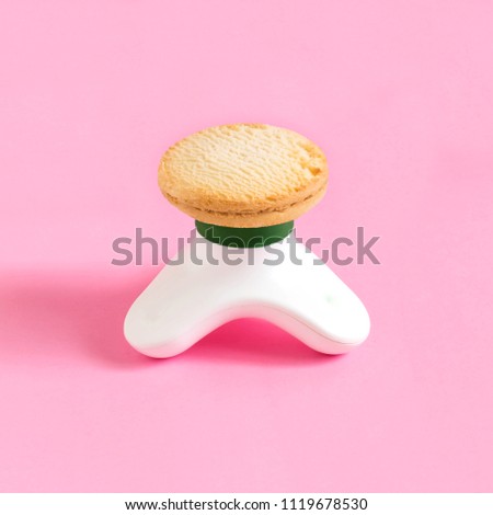 Compact massager and shortbread on pastel pink background. Minimalist style. Creative idea, imagination and fantasy. Attraction of attention to problems of physical inactivity and abuse of sweet