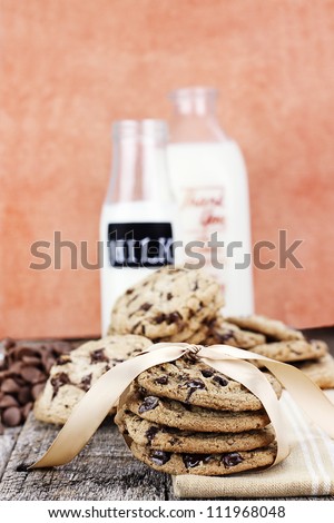 Fresh homemade chocolate chip cookies with chocolate chips and milk in antique milk bottles in the background. Shallow depth of field.