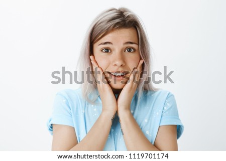 He is man of my dreams. Portrait of passionate impressed cute woman with fair hair in trendy t-shirt, holding palms on cheeks and gazing with loving expression at camera, being amused and romantic