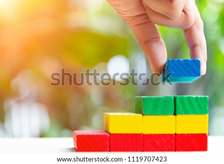 Concepts of building a staircase and step up of wooden pegs for another entrepreneur to climb up the ladder of success.Two finger hold blue block wood last piece for close project. Royalty-Free Stock Photo #1119707423
