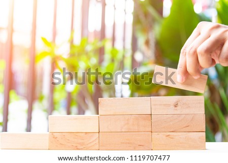 Concepts of building a staircase and step up of wooden pegs for another entrepreneur to climb up the ladder of success.Two finger hold block wood for close project. Royalty-Free Stock Photo #1119707477