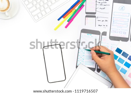 Working desk with hand sketching of screens for mobile responsive website development with UI/UX. Developing wireframe sketch layout design mockup on smartphone screen.