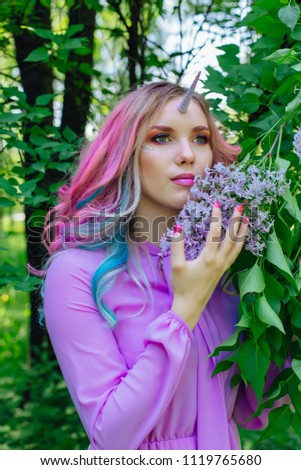 Fairy girl unicorn with rainbow hair and shiny makeup holding lilac flowers.