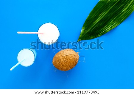 Light cocktail with coconut milk. White tropical beverage in glasses with straw on blue background with coconut and palm leaves top view copy space