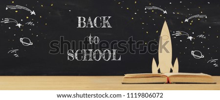Back to school concept. wooden rocket and space sketchs over open book in front of classroom blackboard
