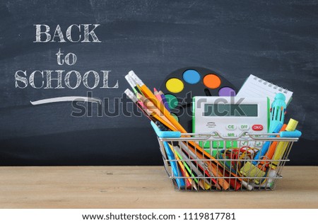 Shopping cart with school supply in front of blackboard. Back to school concept