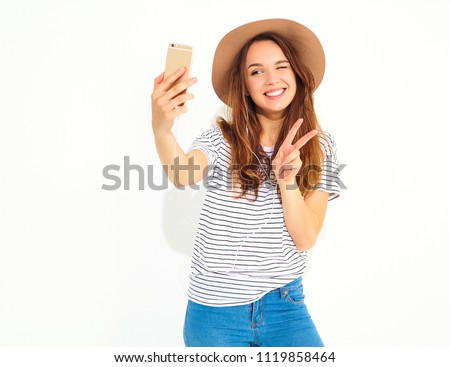 Portrait of a pretty girl in summer hipster clothes taking a selfie isolated on white background. Winking and showing peace sign