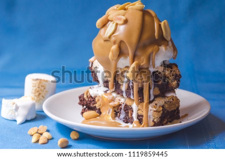The ultimate indulgent and rich peanut butter brownie sundae topped with ice cream, melted peanut butter and nuts shot in front of a blue background Royalty-Free Stock Photo #1119859445
