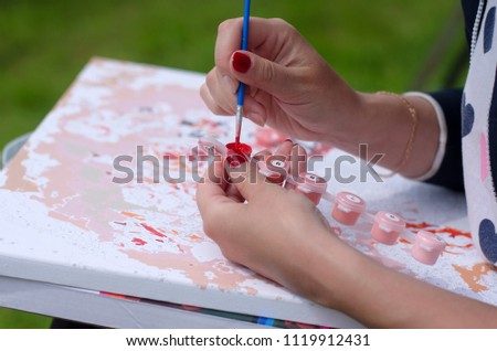 Women's hands with a brush mix red paint on the background of the canvas close-up